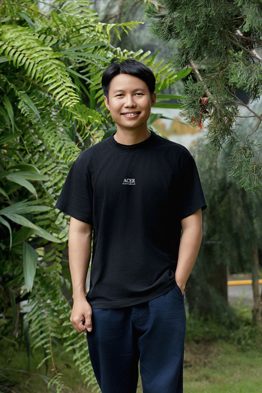 smiling man posing outdoors among greenery